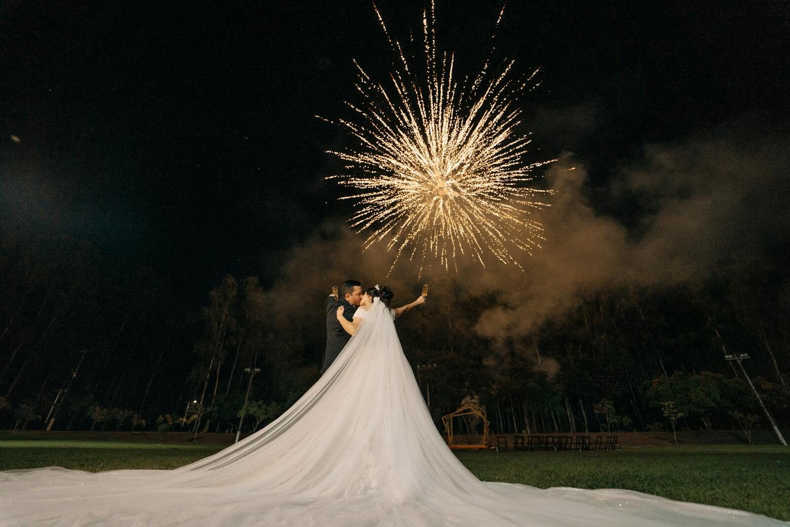 A couple shares a tender moment as fireworks light up the night sky, celebrating their wedding outdoors.